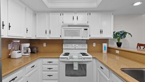 A kitchen with white cabinets, a microwave, a stove, a coffee maker, and a plant. - Beachfront 3BR/3BA condo with Gulf views in South Padre Island. (South Padre Island)