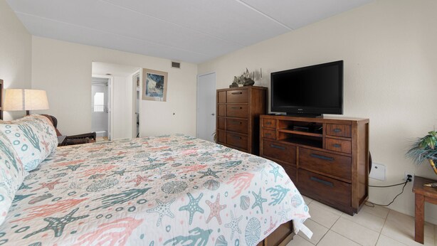 A bedroom with a bed, dresser, TV, and a door leading to another room. - Beachfront 3BR/3BA condo with Gulf views in South Padre Island. (South Padre Island)