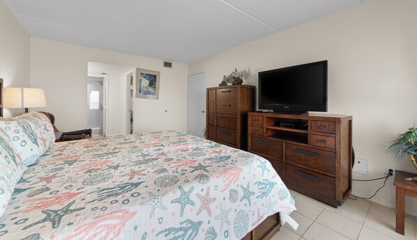 Ein Schlafzimmer mit Bett, Kommode, Fernseher und einer Tür zu einem weiteren Raum.