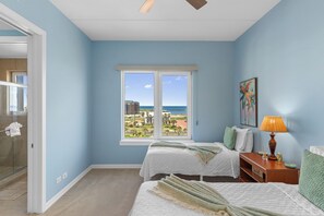Ein Schlafzimmer mit zwei Betten, einem Fenster mit Blick auf Strand und Meer sowie einem Bild an der Wand.