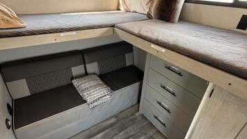 Een ruimtelijk ingerichte camperinrichting met een bed, opbergladen en een raam.