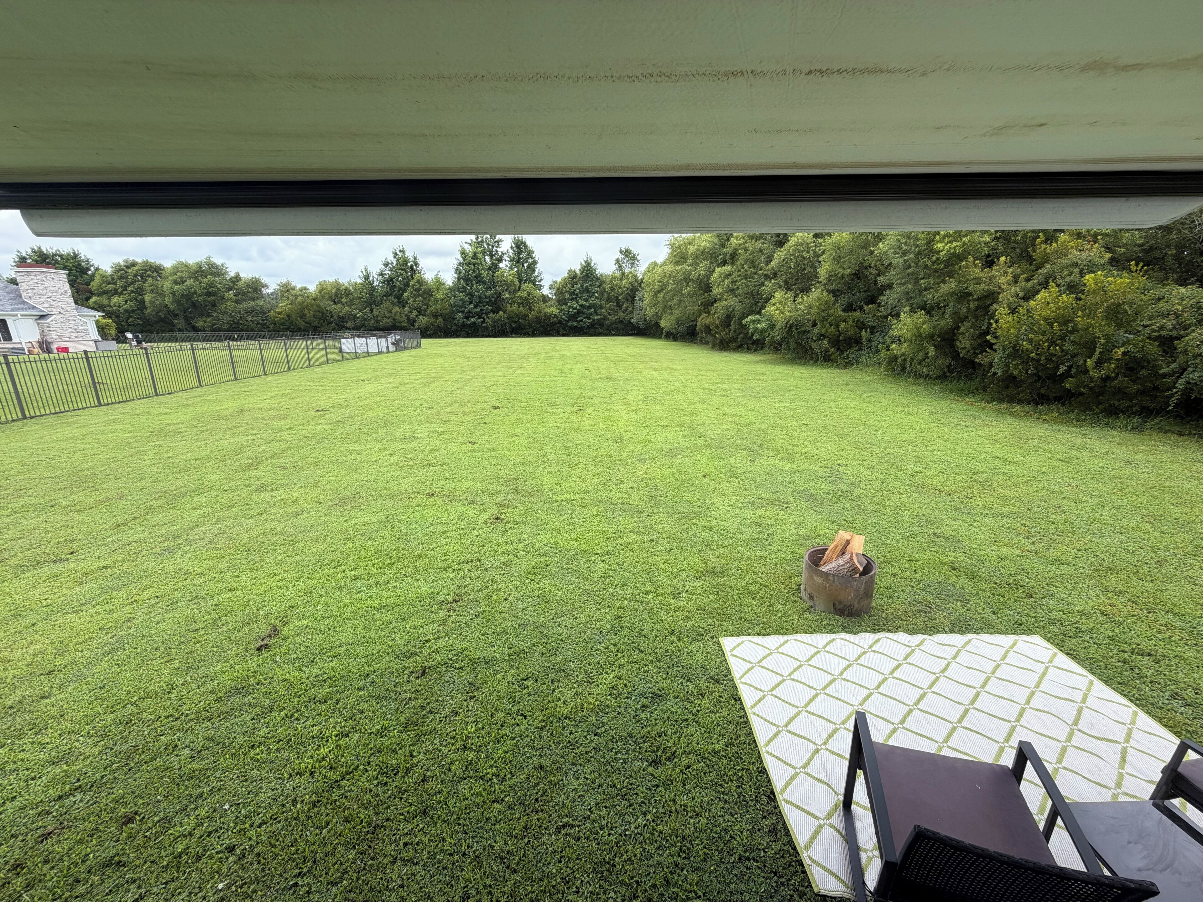 Blick aus einem Fahrzeug auf eine grüne Wiese mit Zaun, Bäumen und einem Gebäude im Hintergrund.