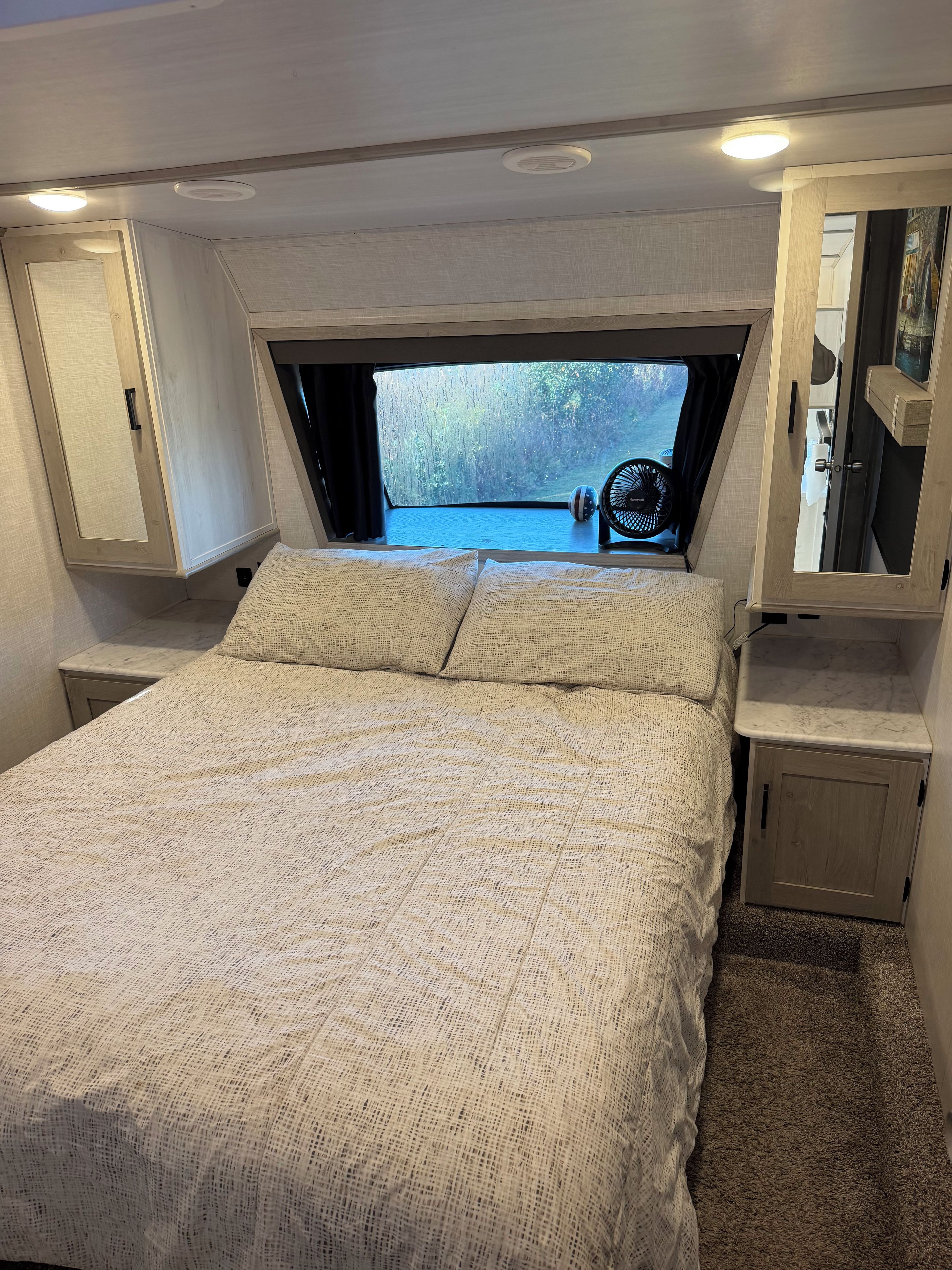 Ein Schlafzimmer mit einem großen Bett, einem kleinen Tisch und einem Fenster mit Blick auf Bäume.