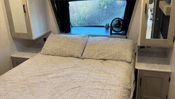 Ein Schlafzimmer mit einem großen Bett, einem kleinen Tisch und einem Fenster mit Blick auf Bäume.