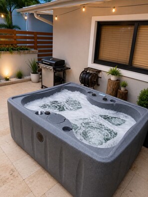 Ein Whirlpool in einem Garten mit Grill und Lichterketten.