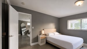 Ein Schlafzimmer mit Bett, Nachttischen, einem Spiegel und einem Fenster mit Jalousien.