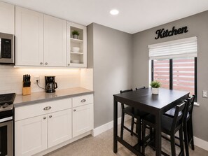 A modern kitchen with white cabinetry, a coffee maker, and a dining table with chairs.