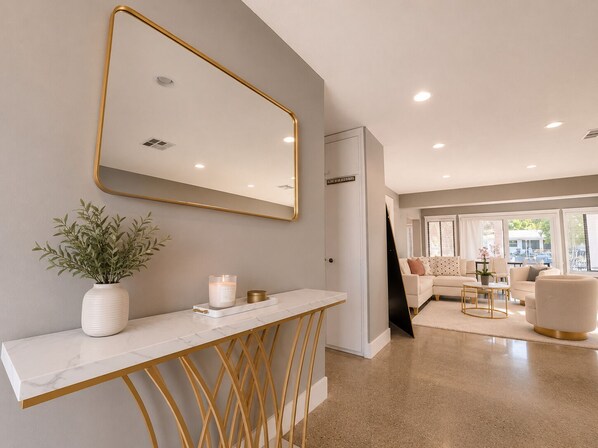 Un intérieur moderne avec une console blanche, un grand miroir et un espace salon comprenant un canapé et des fauteuils.