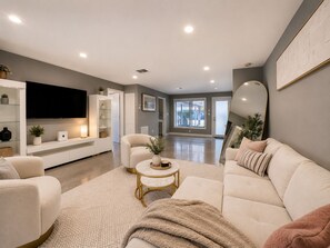 Ein modernes Wohnzimmer mit einer Couch, einem Sessel, einem Couchtisch und einem Flachbildfernseher.