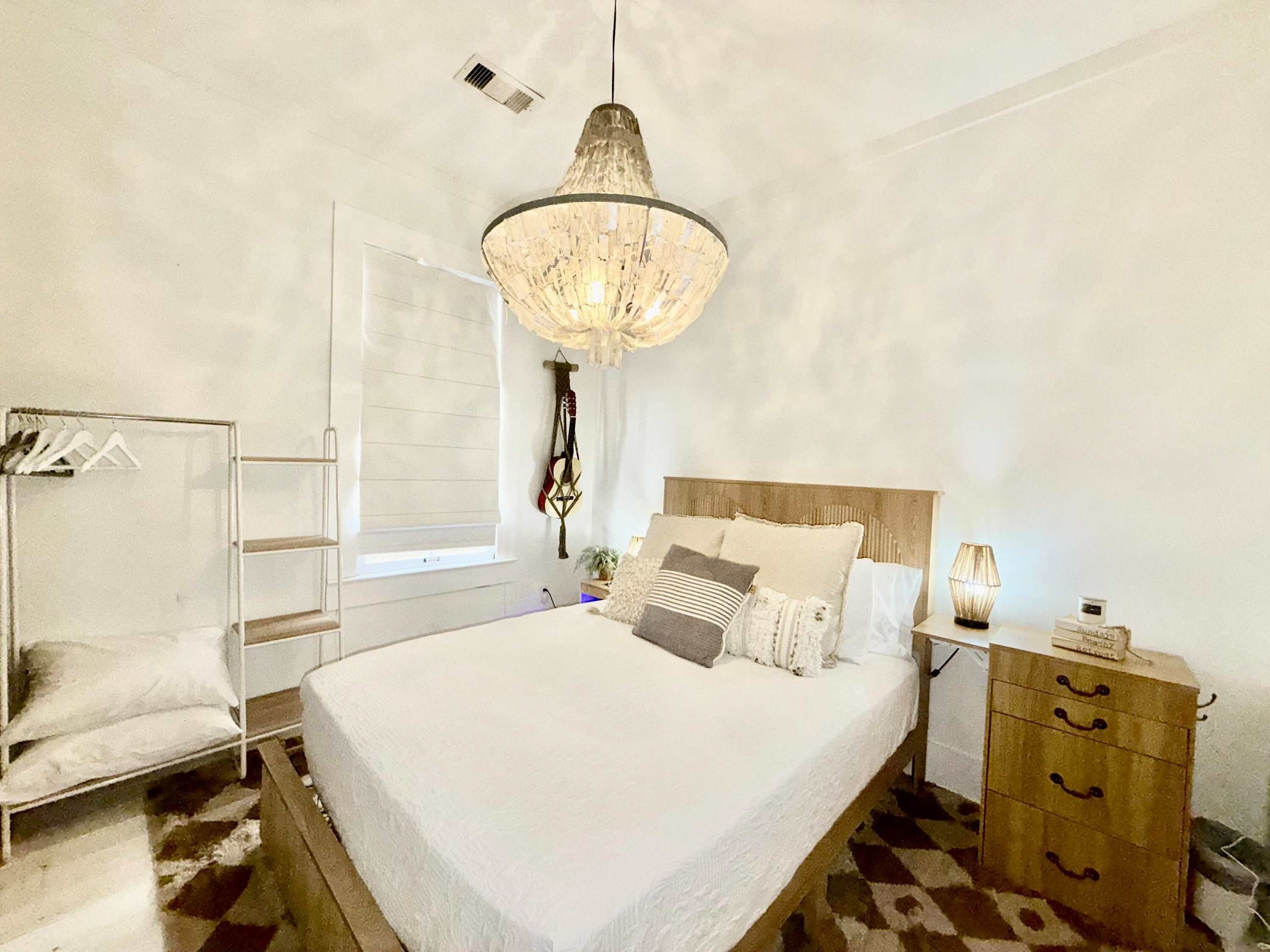 Un dormitorio con una cama, una lámpara colgante, un armario y una ventana con persianas.