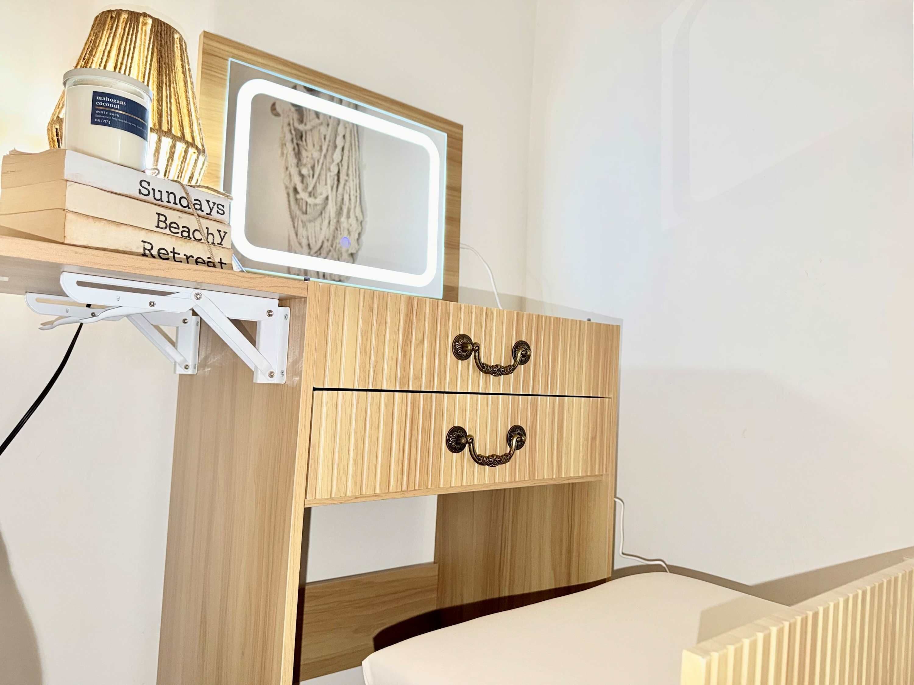 Une table de chevet en bois, avec une lampe blanche, un miroir et une bougie.