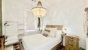 A bedroom with a bed, bedside table, lamp, and a hanging light fixture.