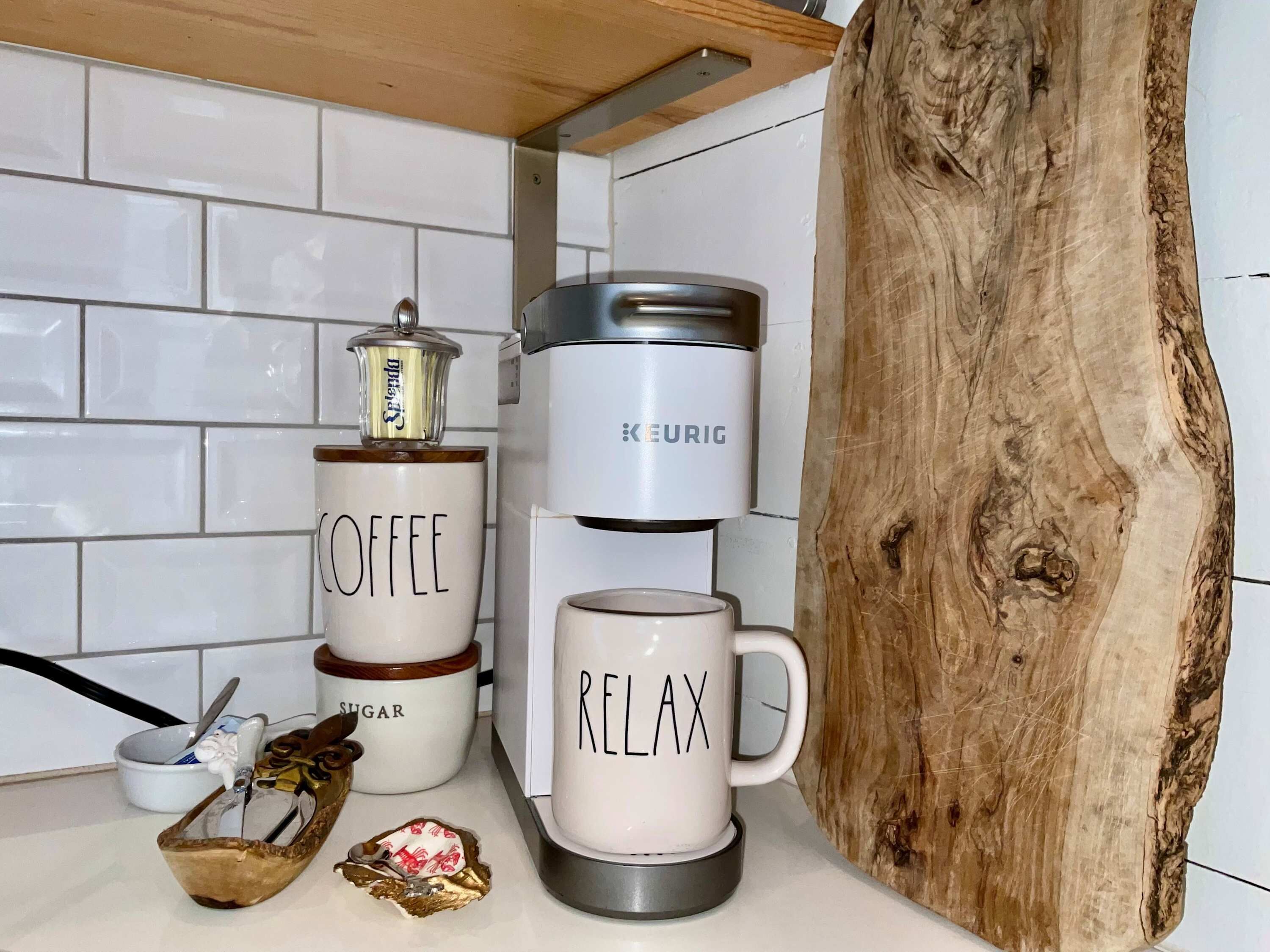 Un piano di lavoro in cucina con una macchina del caffè, una tazza con la scritta 'RELAX' e un contenitore per lo zucchero.