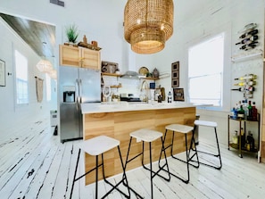 Una cocina moderna con una isla central, taburetes de bar, una lámpara colgante y botellas de vino en la pared.