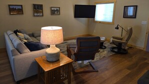Ein Wohnzimmer mit einer Couch, einem Sessel, einer Lampe, einem Flachbildfernseher und gerahmten Bildern an der Wand.
