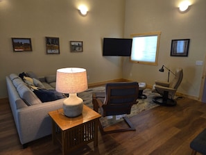 A living room with a sofa, a chair, a lamp, a flat-screen TV, and framed pictures on the wall. - Shell Lake Getaway. Spacious 3-bedroom barndominium in nearby Beaver Brook (Shell Lake)