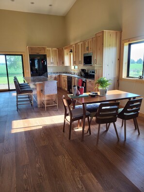 A modern kitchen with wooden cabinets, a central island, and a dining area with chairs. - Shell Lake Getaway. Spacious 3-bedroom barndominium in nearby Beaver Brook (Shell Lake)