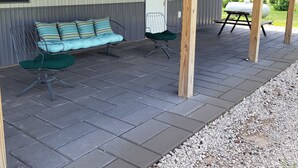 Ein überdachter Patio-Bereich mit einer Bank, einem Stuhl und einem Grill.