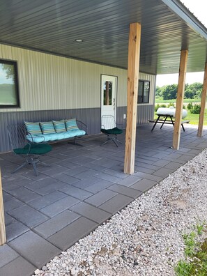 A covered patio area with a bench, a chair, and a grill. - Shell Lake Getaway. Spacious 3-bedroom barndominium in nearby Beaver Brook (Shell Lake)