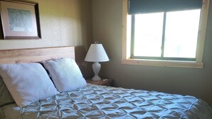 Ein Schlafzimmer mit einem Bett, einem Nachttisch, einer Lampe, einem Fenster und einem Bild an der Wand.