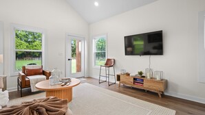 A modern living room with a flat-screen TV mounted on the wall, a wooden coffee table, a brown leather sofa, and a glass coffee table. - Thors Cottage at Hidden Gem Farm-Sleeps 5 (Spring Hill)