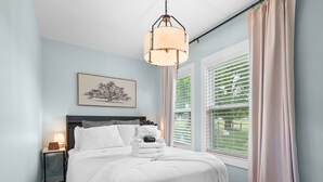 A neatly made bed with a white comforter and pillows, a bedside table with a lamp, a framed picture on the wall, and a window with blinds. - Thors Cottage at Hidden Gem Farm-Sleeps 5 (Spring Hill)