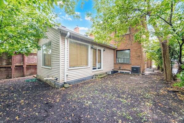 A single-story house with a brick exterior, a covered porch, and a yard with mulch and young plants.