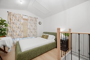 A bedroom with a bed, a bedside table, a potted plant, and a window with curtains.