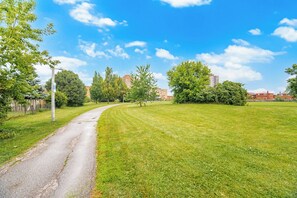 A paved pathway curving through a well-maintained grassy area with trees and a clear blue sky.