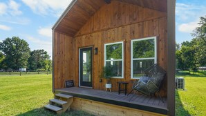 A wooden cabin with a porch, a door, and two windows. - The Music Box at Hidden Gem Farm-Sleeps 6 (Spring Hill)
