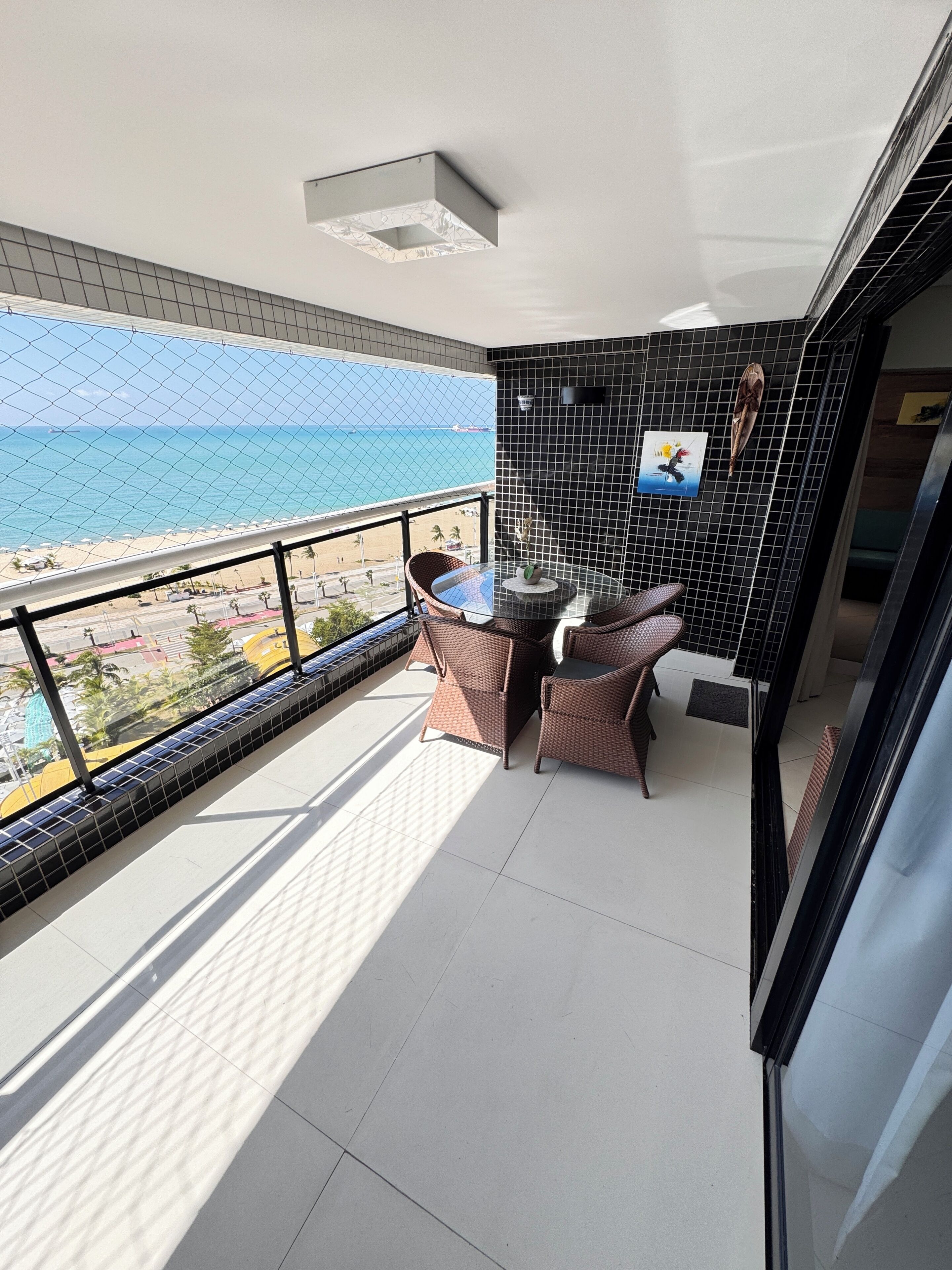A balcony with a view of the beach, wicker furniture, and a tiled wall.