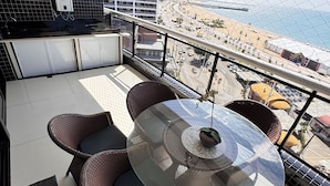 A balcony with wicker furniture, a glass table, and a view of a beach and cityscape. - Hotel Platinum Landscape Luxo apartment (Fortaleza)