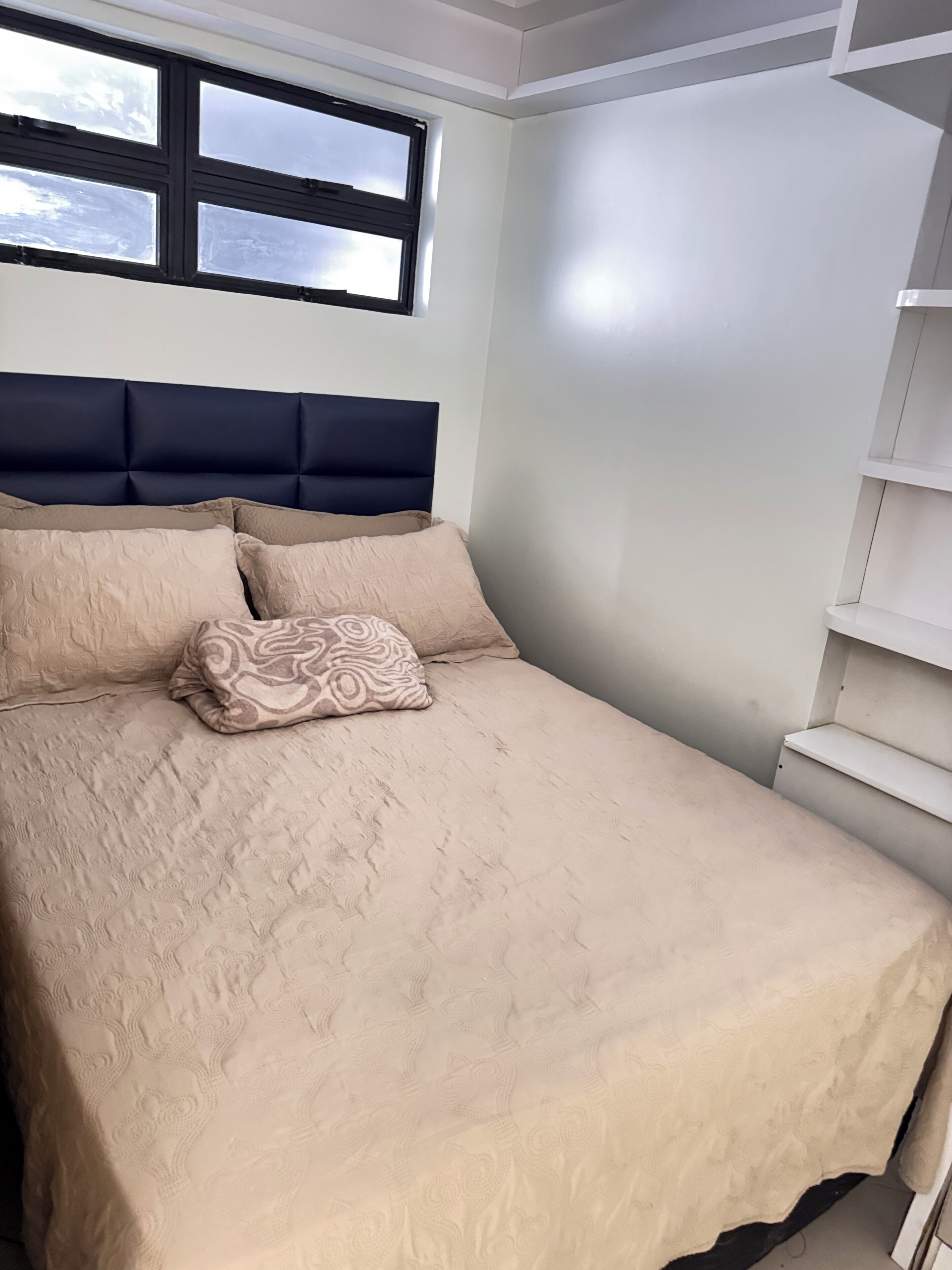 Ein Schlafzimmer mit Bett, Kopfteil, Fenster und einer weißen Wand.