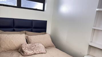 Ein Schlafzimmer mit Bett, Kopfteil, Fenster und einer weißen Wand.