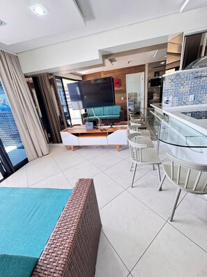 Une chambre d’hôtel moderne dotée d’une grande télévision à écran plat, d’un canapé, d’un coin repas avec une table en verre et d’un balcon avec vue.
