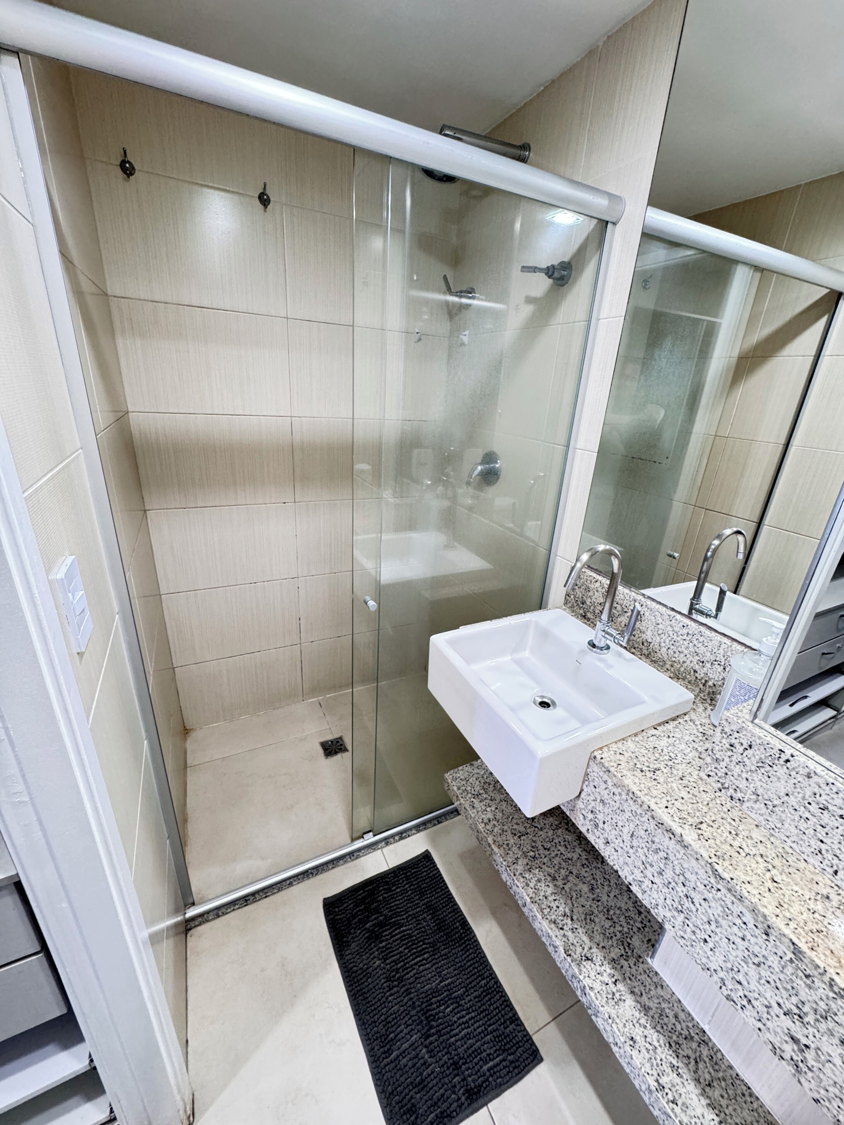 Un baño moderno con cabina de ducha de vidrio, un lavamanos blanco y encimera de granito.