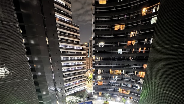 A high-rise building with multiple floors, a central courtyard with palm trees, and a green-lit pathway. - Hotel Platinum Landscape Luxo apartment (Fortaleza)