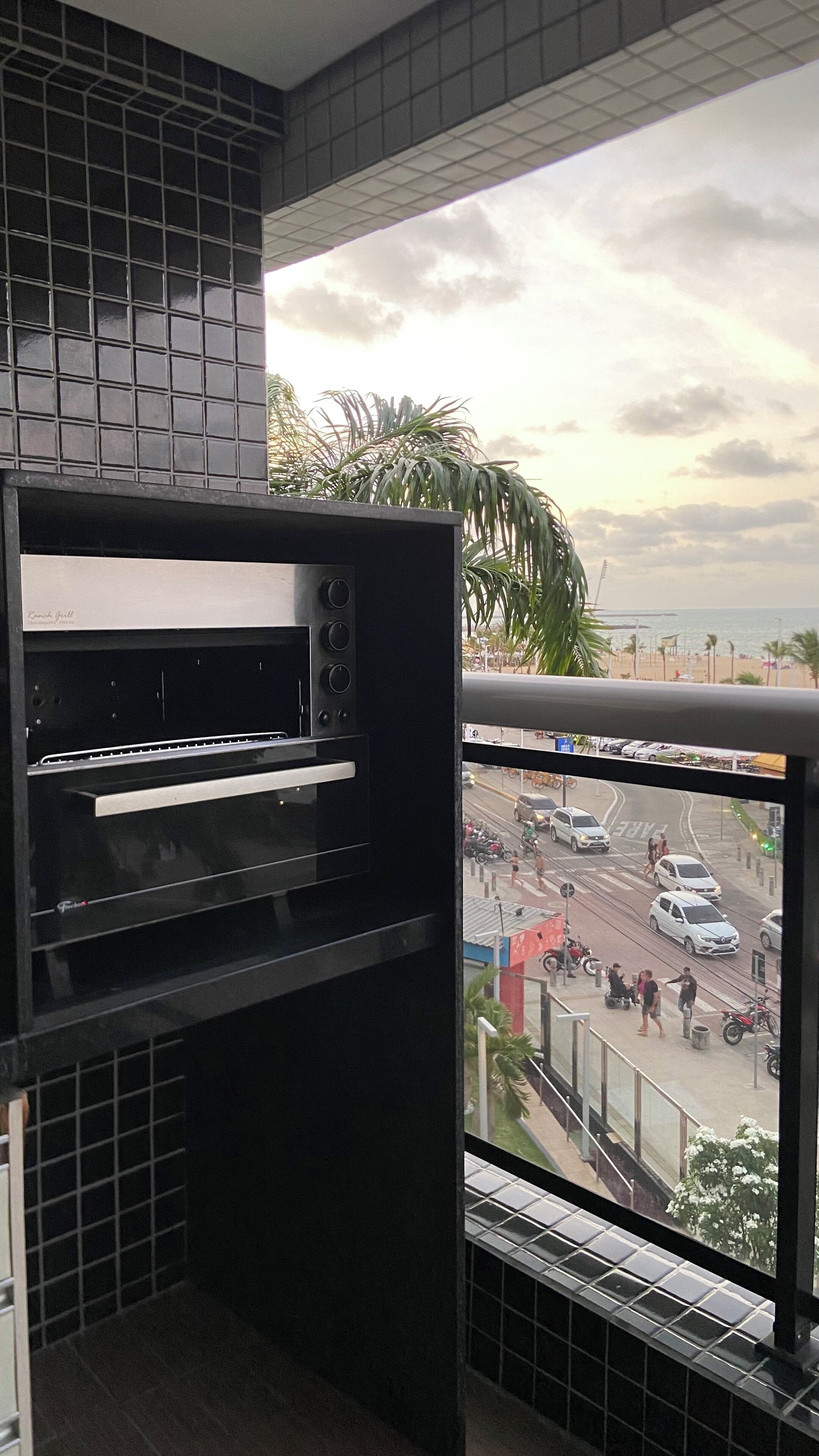 Een keuken met een inbouwoven en uitzicht op een drukke straat met palmbomen en een strand op de achtergrond.