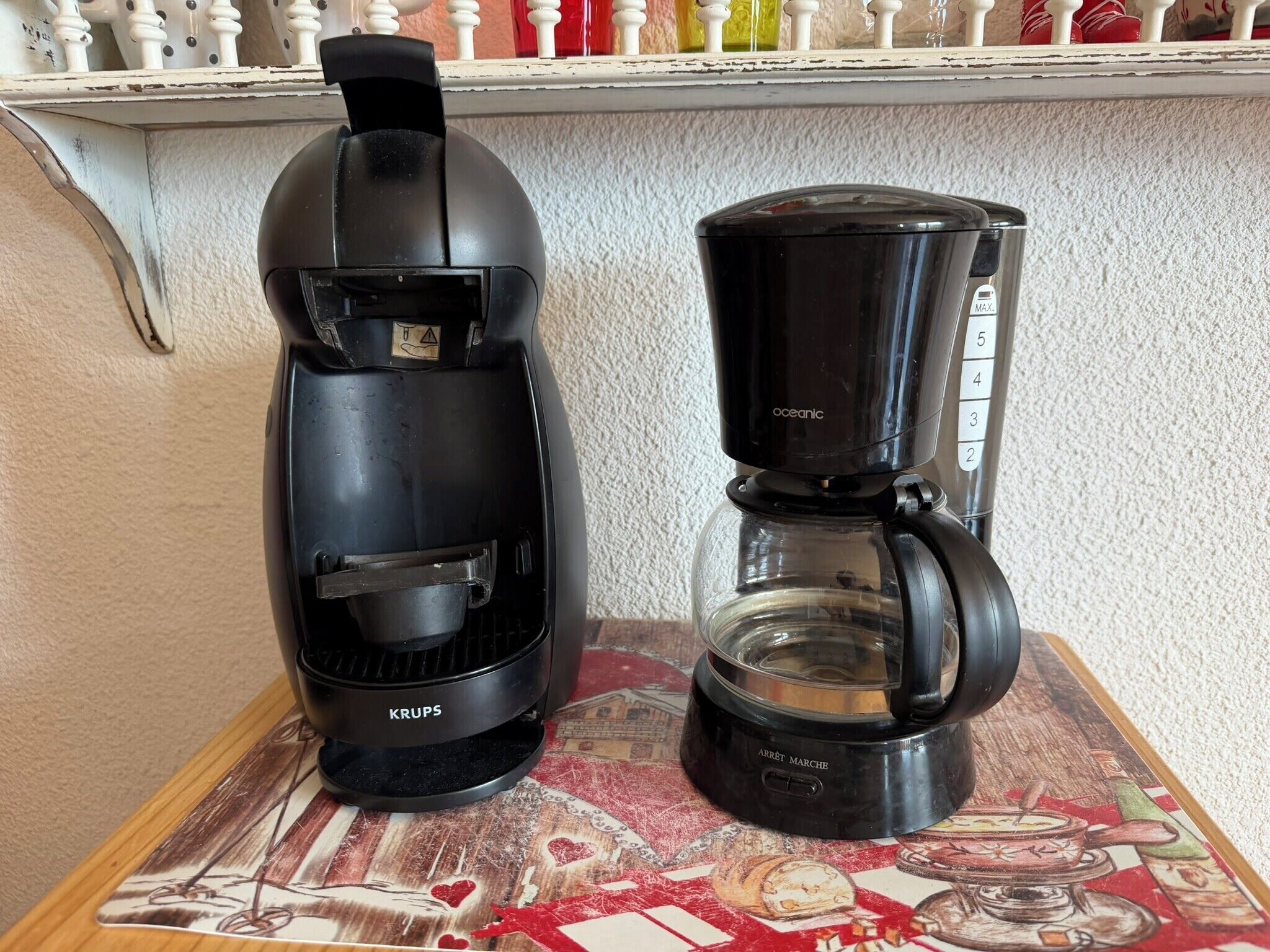 Två kaffebryggare står på ett bord med ett mönstrat bordsduksöverdrag.