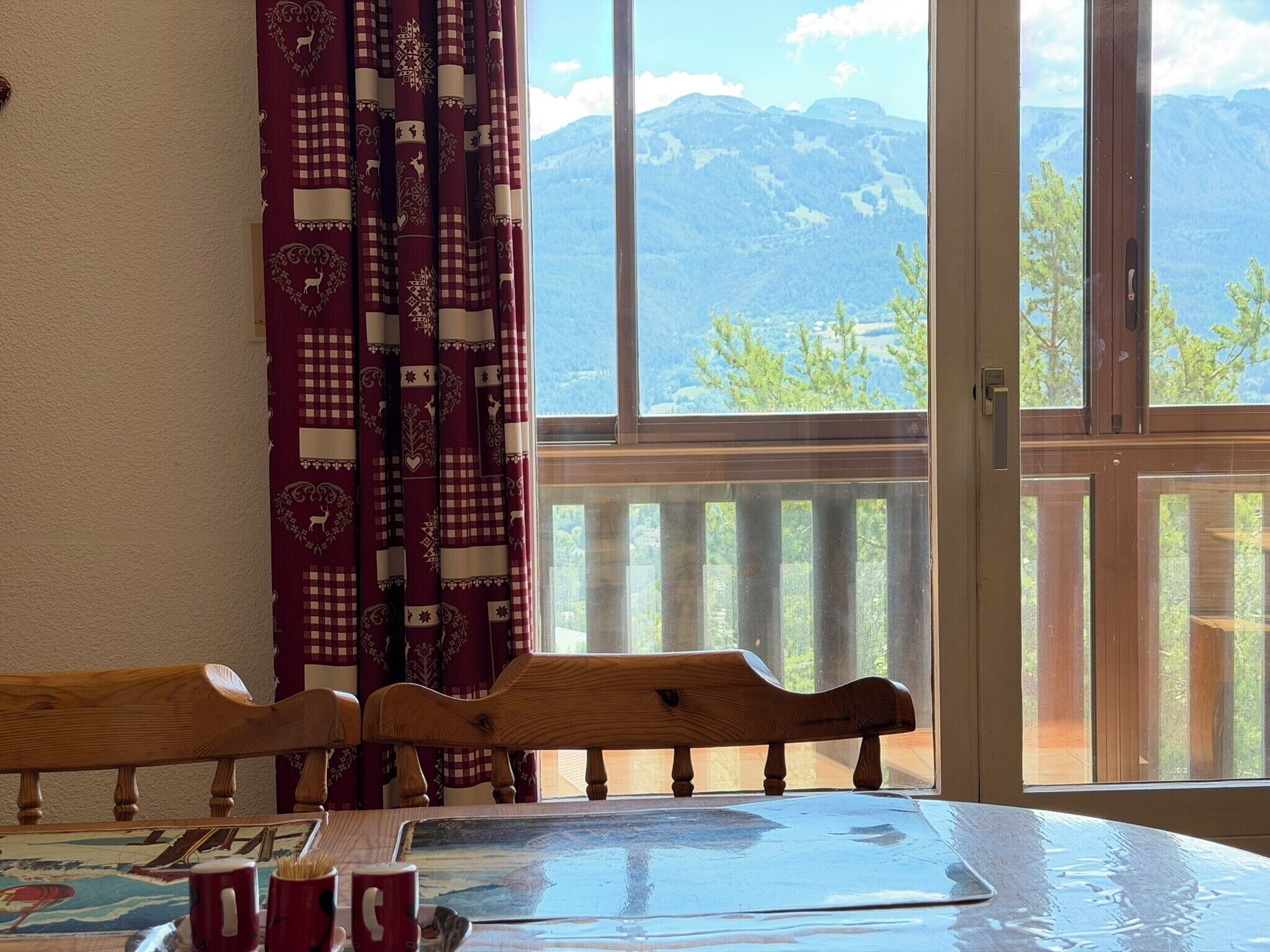 A room with a large window, wooden chairs, a table, and a view of mountains.