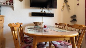 Ein Essbereich mit Holztisch, Stühlen, einem an der Wand befestigten Fernseher und einem Regal mit Dekoration.