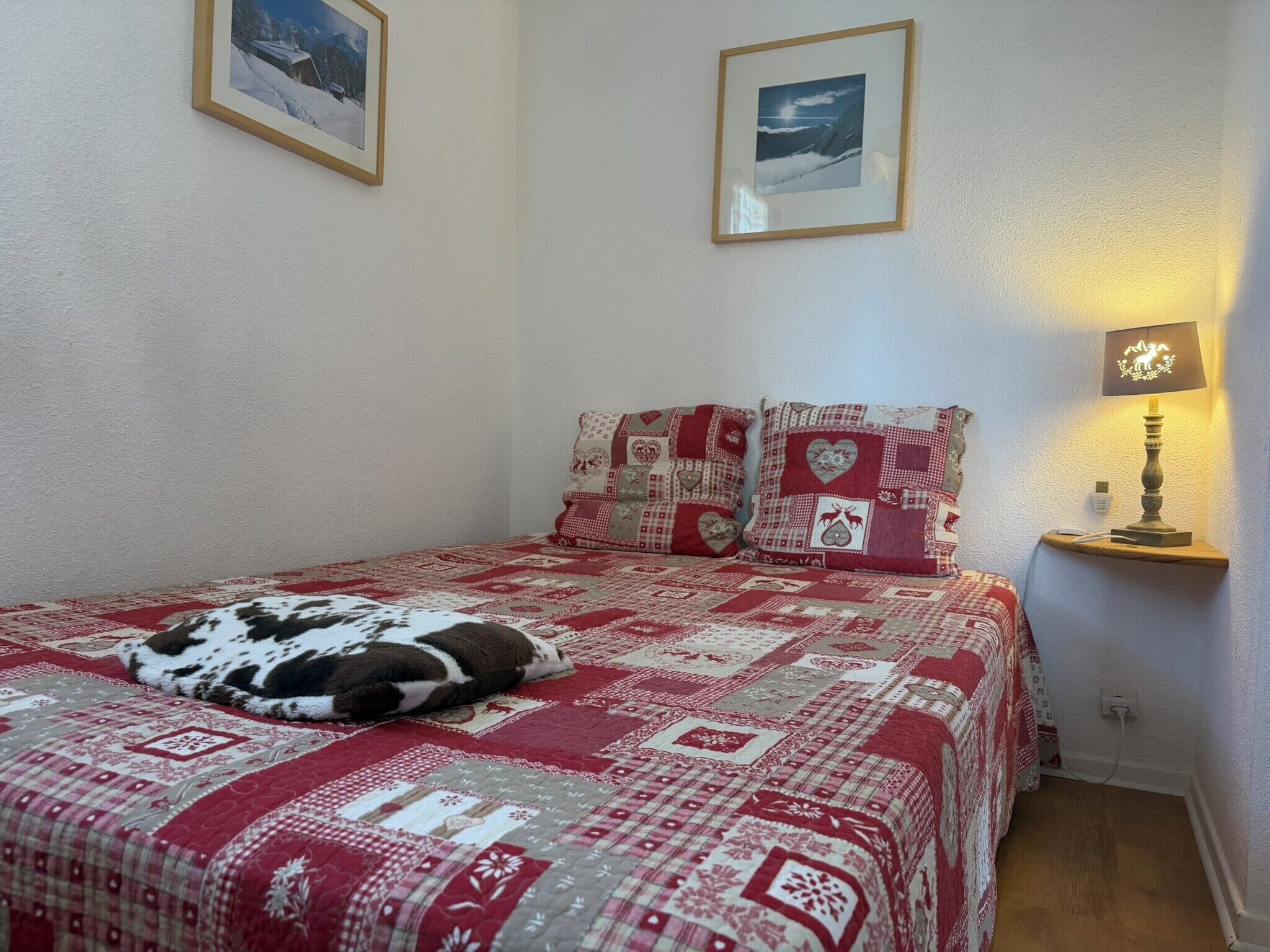 A bedroom with a bed, pillows, a bedside lamp, and two framed pictures on the wall.