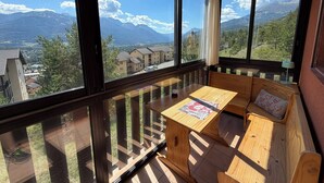 Ein Balkon mit Holztisch und Bank, der Blick auf Berge und eine Stadt gewährt.