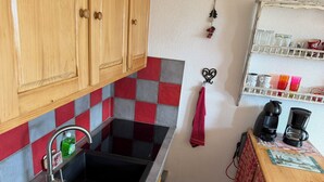 Eine Küche mit Holzschränken, einer gefliesten Spritzschutzwand, einem Spülbecken, einer Kaffeemaschine und einem Regal mit Tassen.