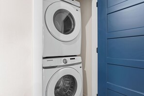 A stacked washer and dryer unit in a laundry room with a blue door. - TaneyComo Wake & Lake (Branson)