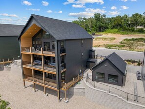 A multi-story building with a balcony on the ground floor, a separate smaller building attached to the main structure, and a gravel driveway. - TaneyComo Wake & Lake (Branson)