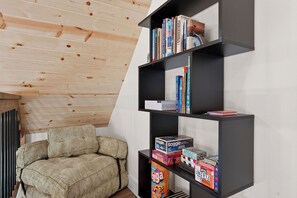 Een modern interieur met een houten schuine daklijn, een zwarte boekenkast met boeken en spellen, en een gestructureerde bank.
