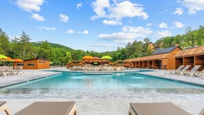 A pool area with lounge chairs and umbrellas, surrounded by wooden buildings and trees. - Not So Crappie Cabin - 3BR/3BA, Private Hot Tub, Resort Pools & Lazy River (Hollister)