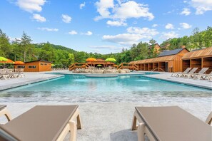 A pool area with lounge chairs and umbrellas, surrounded by wooden buildings and trees. - Not So Crappie Cabin - 3BR/3BA, Private Hot Tub, Resort Pools & Lazy River (Hollister)