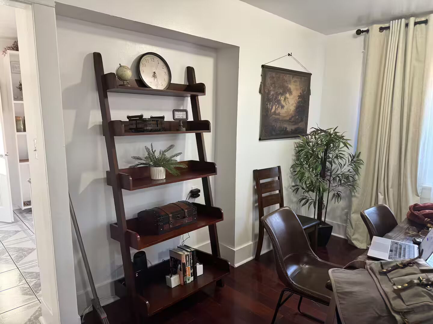 Una sala de estar con una estantería de madera, un cuadro, una planta en maceta y un comedor con sillas y una mesa.
